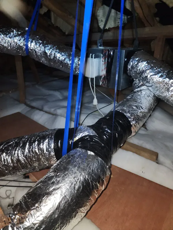 Black and silver ducting joined at a fitting, hung on blue straps in a roof space