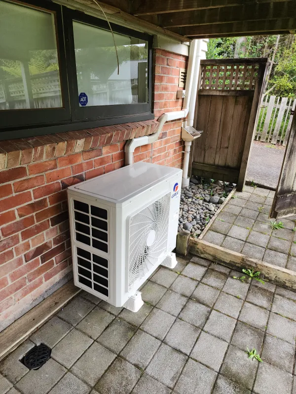 Large ducted heat pump outdoor unit on a concrete pad beside a house