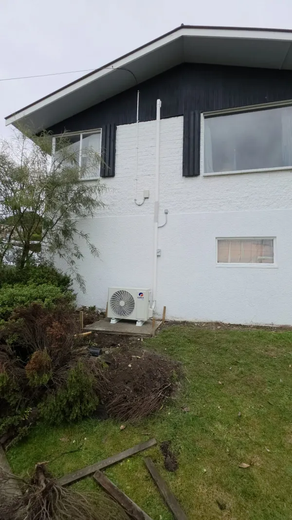 Ducted heat pump outdoor unit on a concrete pad beside a fence