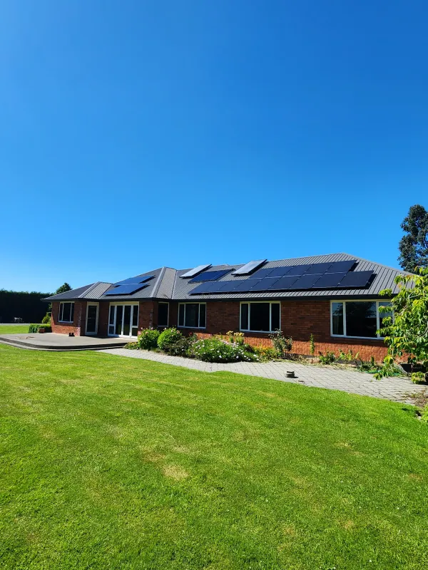 Brick home with dark roof panels across a wide green lawn