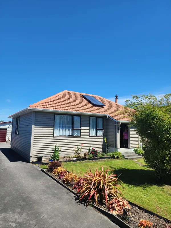 Weatherboard home with a red tiled roof and a solar air panel, under a clear blue sky