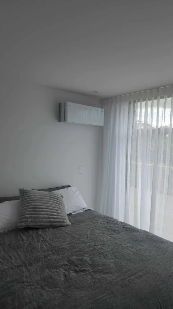 Bedroom with a white high wall heat pump above sheer curtains