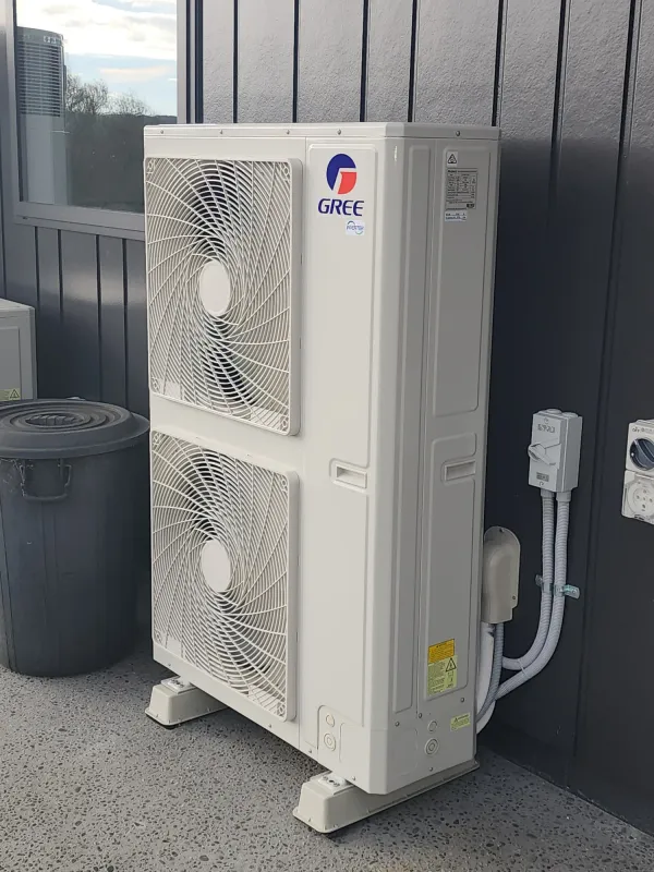 Ducted heat pump outdoor unit on pavers beside a timber fence