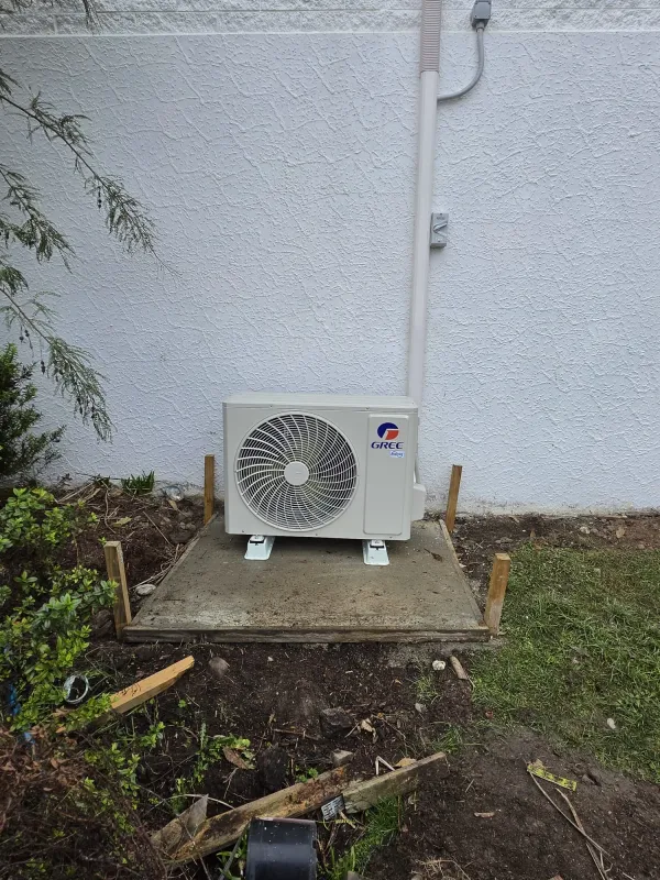 Compact Gree outdoor unit on a fresh concrete pad against a white wall