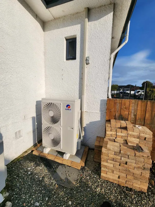 Ducted heat pump outdoor unit on a gravel pad beside a house