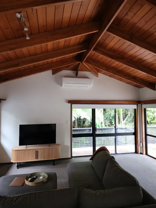 Lounge with a timber cathedral ceiling and a white high wall heat pump above the sliding doors