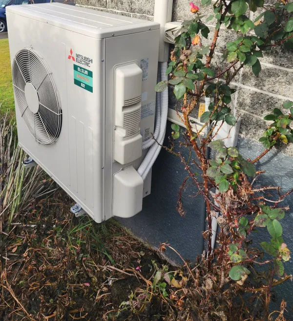 Mitsubishi Electric outdoor unit mounted on a wall beside garden plants