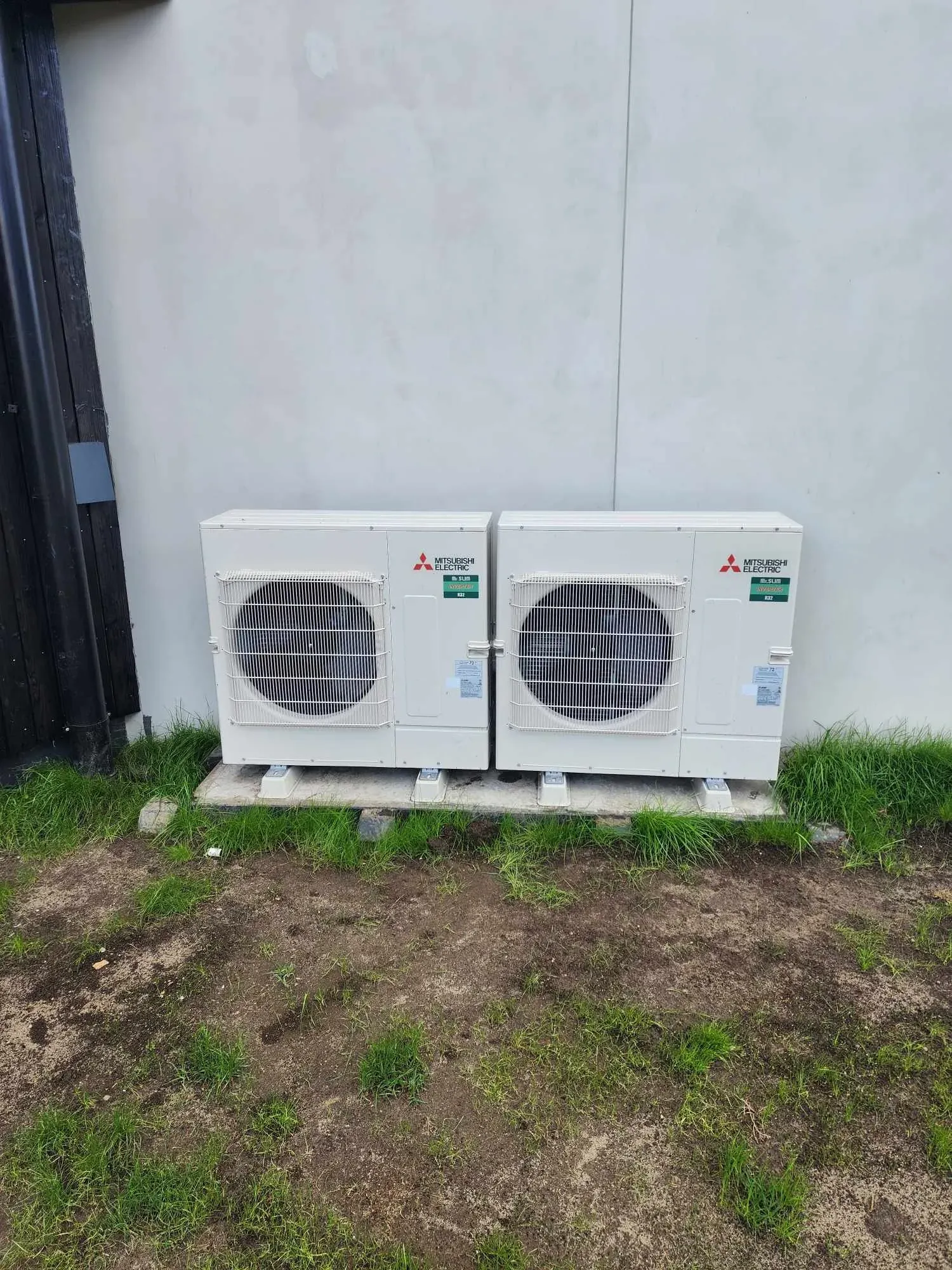 Two outdoor heat pump units against a white wall