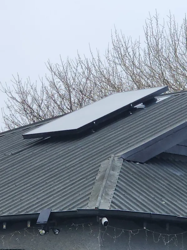 Solar air panel mounted on a dark roof with bare winter trees behind