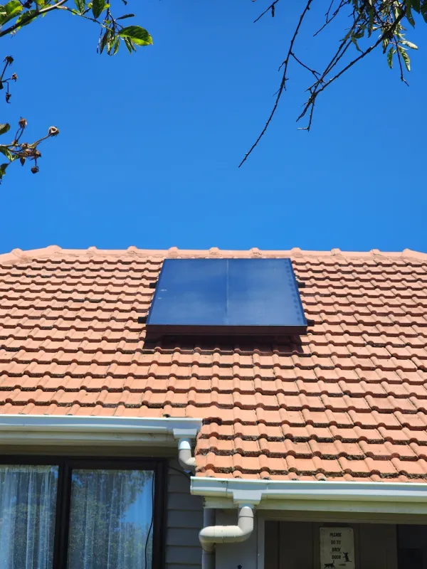 Dark solar air panel set into a terracotta tiled roof above a gutter