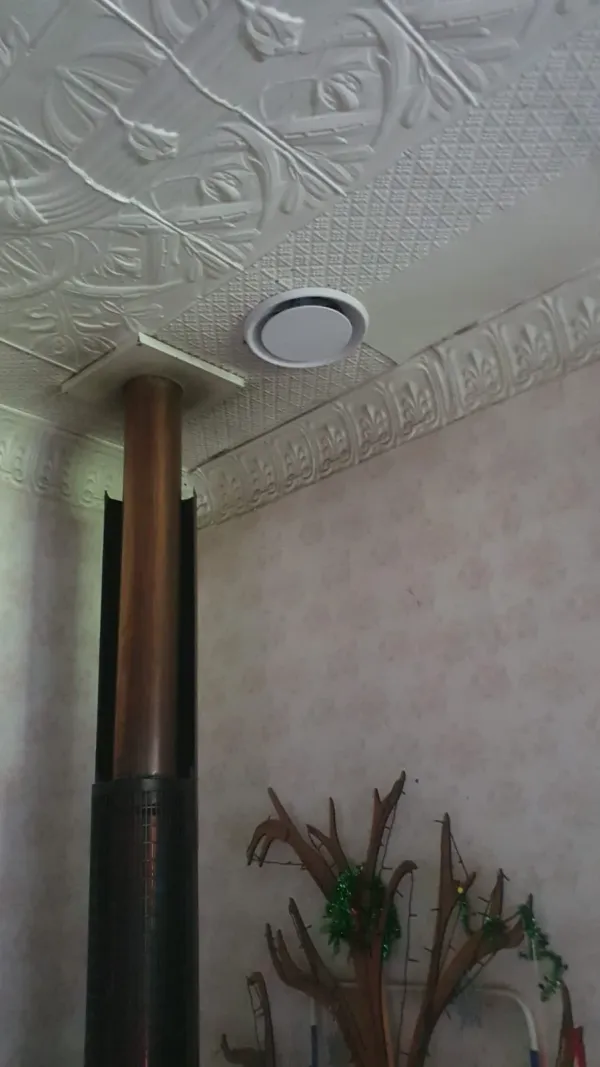 Round heat transfer outlet grille set into a ceiling near a wood burner flue