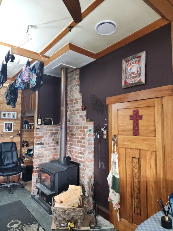 Round heat transfer outlet grille in the ceiling above a wood burner and brick chimney