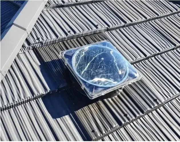 Clear sun tube dome fitted among grey roof tiles